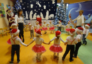 Pani dyrektor Maria Królikowska i pani Ewelina Cicha tańczą z dziećmi w kółeczku.